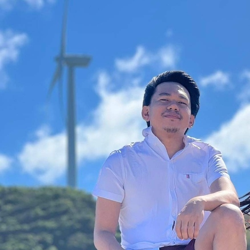 A person sitting with windmill background and a blue sky.